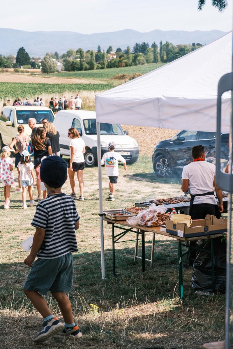 Un enfant regarde un stand de barbecue sous un barnum, au milieu des convives